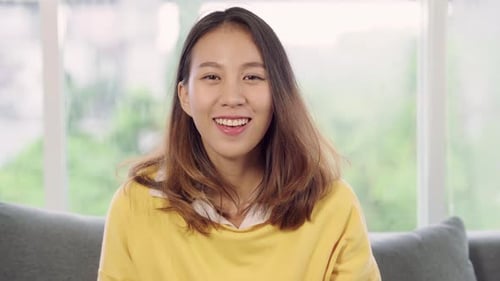 Asian woman feeling happy smiling and looking to camera while relax in her living room at home.