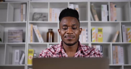 Man Working on Laptop in Front of Bookshelf