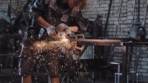 Junger Mann arbeitet im Werk und schneidet das Metallstück mit einem Winkelschleifer ab