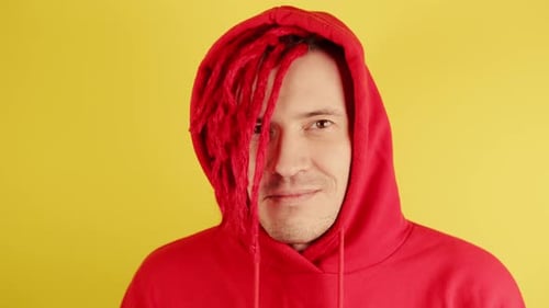 Young Man with Red Dreadlocks in Hood Looks at Camera and Winks