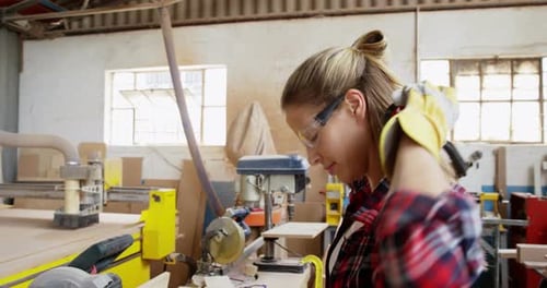 Woman Removing Safety Gear in Woodworking Workshop