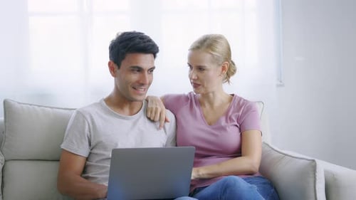 Smiling Couple Using Laptop on Couch at Home
