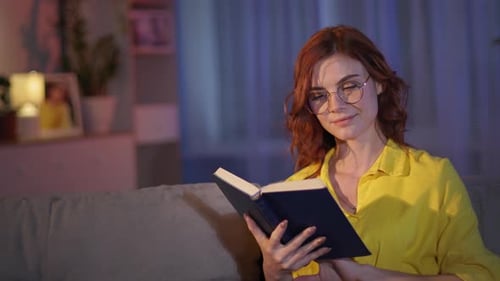 Woman Reading Book and Smiling on Sofa