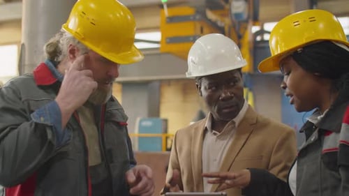 Engineer Using Tablet and Speaking with Factory Technicians