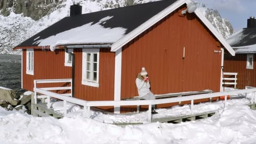 Woman Sits at Cabin in Snowy Landscape