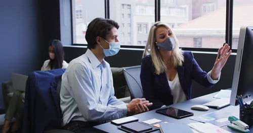 Diverse business people wearing face masks using computer in office