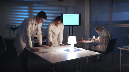 Colleagues Reviewing Blueprint in Workplace at Night