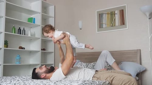 Happy Father Lifts Laughing Baby on Bed