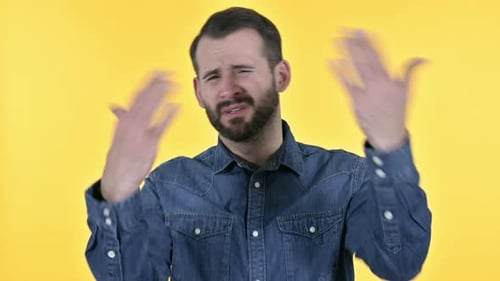 Hombre joven con barba decepcionada que reacciona al fracaso, fondo amarillo