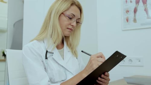 Female Doctor Writing on Clipboard in Office