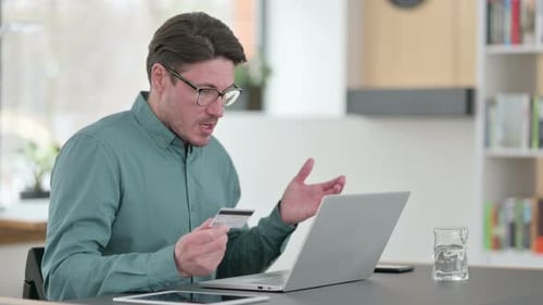Man Holding Credit Card Using Laptop At Desk