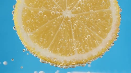 Lemon Slice Submerged in Bubbles on Blue Background