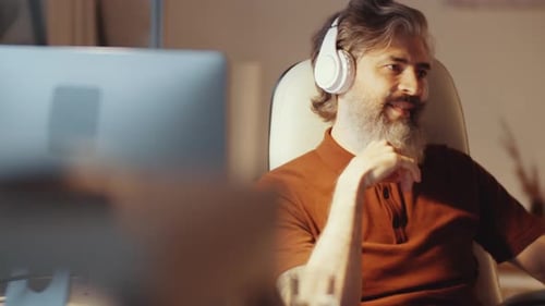 Mid-Aged Bearded Businessman Listening to Music with Headphones in Office