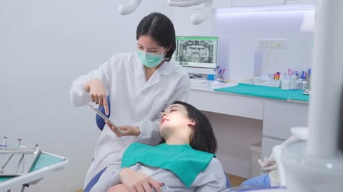 Asiatische junge Zahnärztin hält ein digitales Tablet in der Hand und berät Patienten in der Zahnklinik.