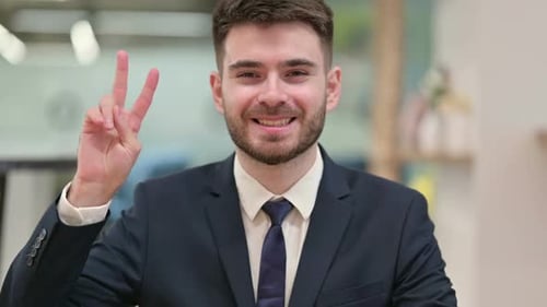Smiling Man Makes Peace Sign in an Office