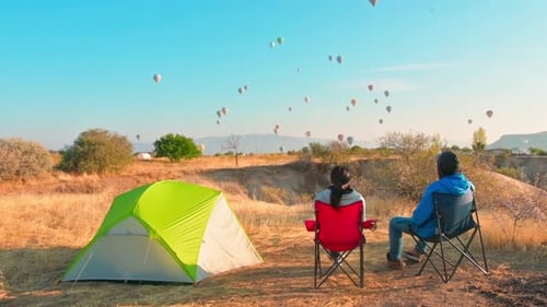 Couple Camping and Watching Hot Air Balloons Soar