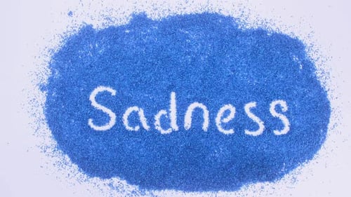 Hand Writes Word Sadness on Blue Background