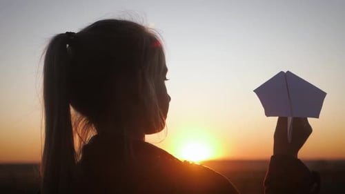Girl Holding a Paper Airplane at Sunset