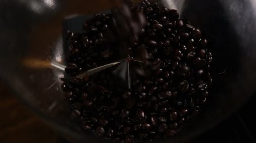 Dunkel geröstete Kaffeebohnen fallen in die Mühle, Ansicht von oben, Zeitlupe