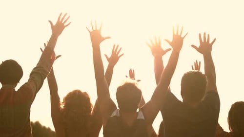 Silhouettes of People with Raised Hands at Sunset