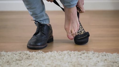 Close-up of Caucasian Adult Man Putting on Men's Broggi Boot and Women's High Heel Shoe