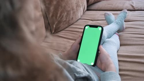 Girl is holding a smartphone in her hands with a green screen for keying.
