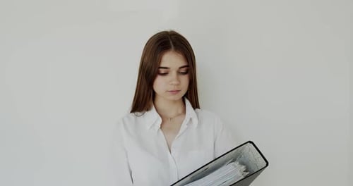 Young Woman Holding Binder Smiling in Front of Wall