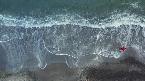 Drohnenschuss eines Mannes, der auf den Färöern am Strand entlang