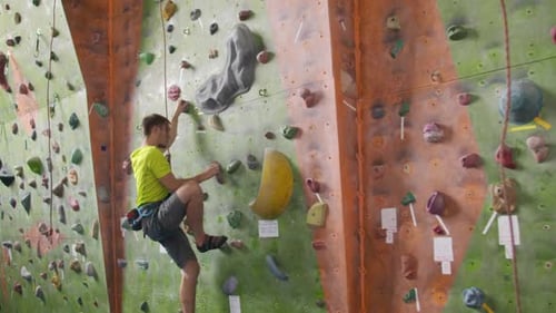 Male Climber Climbs the Cliff Wall in the Room Reaching and Gripping Hold