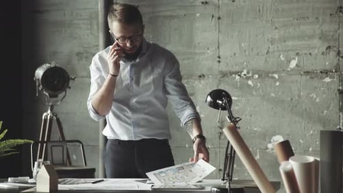 Un homme qui réussit parle au téléphone, garde les plans entre les mains