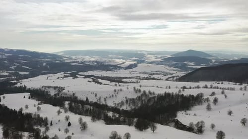 Breite Luftaufnahme der Winterlandschaft; Berge, Tal, spärlicher Wald.