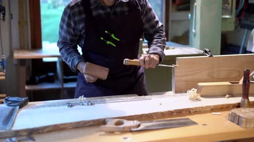 Professional carpenter with hammer and chisel working in workshop