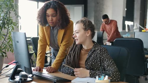 Businesswomen Talking Pointing at Computer Screen Discussing Work in Open Plan Office
