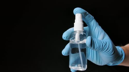 Gloved Hand Sprays Bottle of Disinfectant on Black