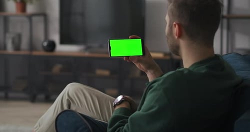 Adult Man Is Resting at Home and Communicating By Video Conference on Display of Smartphone Green