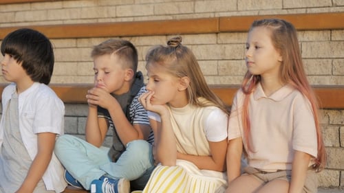 Tired and exhausted primary school kids sitting outdoors.