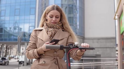 Woman Using Phone While Holding Electric Scooter