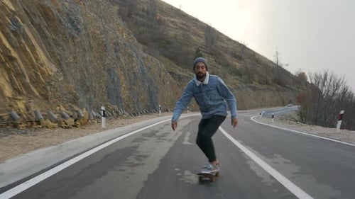 Young Man with a Beard Riding Skateboard Cruising Downhill on Countryside Road