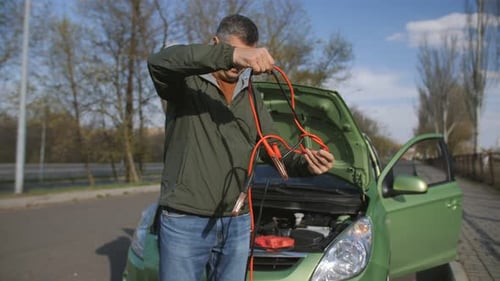 Man Untangling Jumper Cables Beside Car on Road