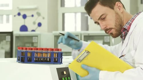 Un joven asistente de laboratorio saca tubos de ensayo con análisis y reescribe los datos sobre ellos