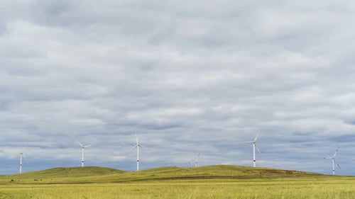 Blades of a Large Wind Turbine in a Field Against a Background of Cloudy Blue Sky on the Horizon