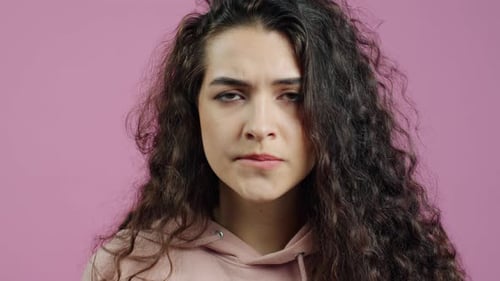 Closeup Portrait of Nervous Young Woman Crossing Fingers and Praying Against Pink Color Background