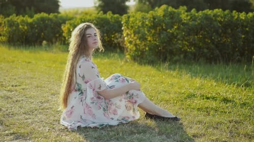 Woman Sits in Sunny Meadow Wearing Floral Dress