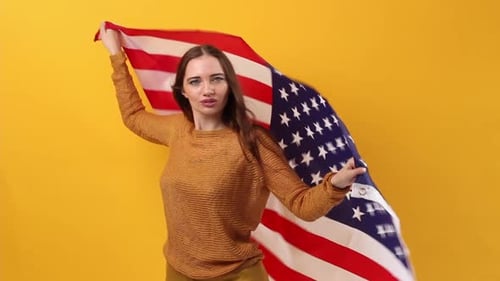 Woman Waving American Flag Against Yellow Backdrop