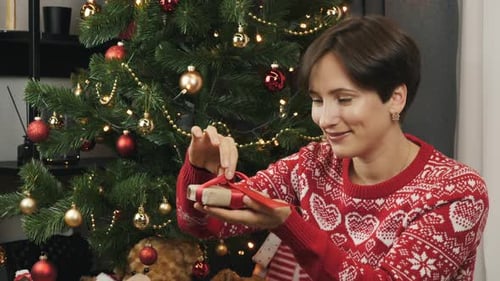 Woman Unties Ribbon on Christmas Gift Near Tree