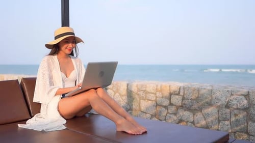 Woman Using Laptop on Lounge Chair at Beach