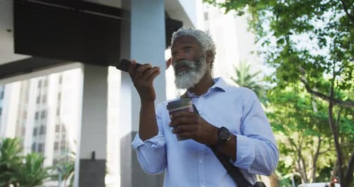 African american senior man drinking coffee and talking on smartphone in corporate park