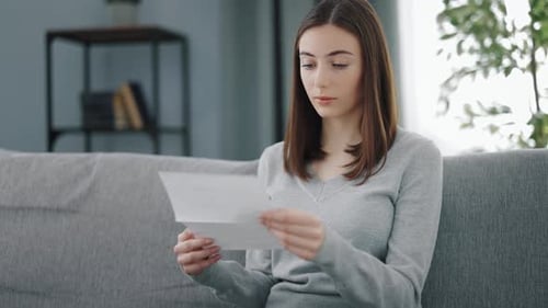 Woman Reading Letter on Couch Indoors During Daytime
