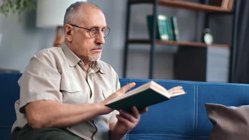 Senior Man Reading Book on Couch at Home
