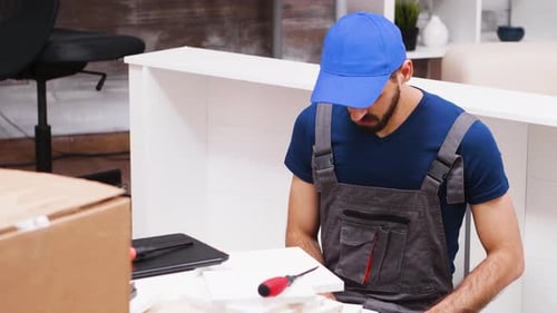 Close Up of Young Man in Coverall Using Laptop To Assembly Furniture